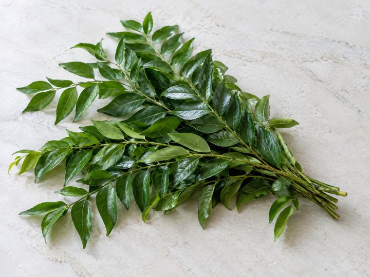 Fresh curry leaf sprigs on a pale surface