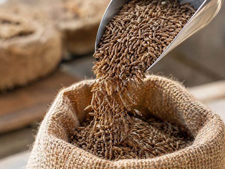 Cumin seeds pouring from a steel scoop into an open jute sack